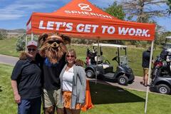 A man and a woman with a bear mascot posing on a golf course